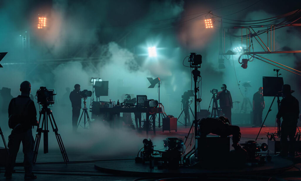A team of individuals works together in a dark room, illuminated by lights and surrounded by filmmaking equipment.